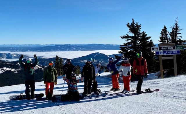 Luxury Mountain Vacation Rentals staff take a group photo in their ski and snowboarding gear while standing on the snowy slopes of Big White Ski Resort.