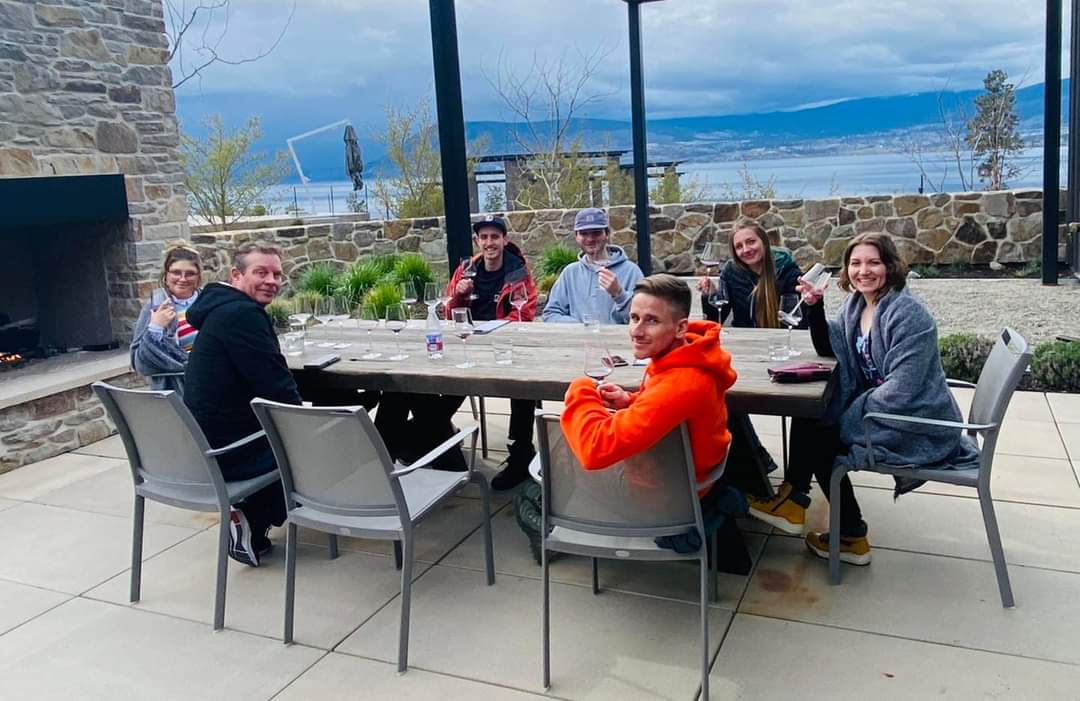 The Luxury Mountain Vacation Rentals staff sit at a patio table overlooking a view of the valley at a staff part on Big White Ski Resort.