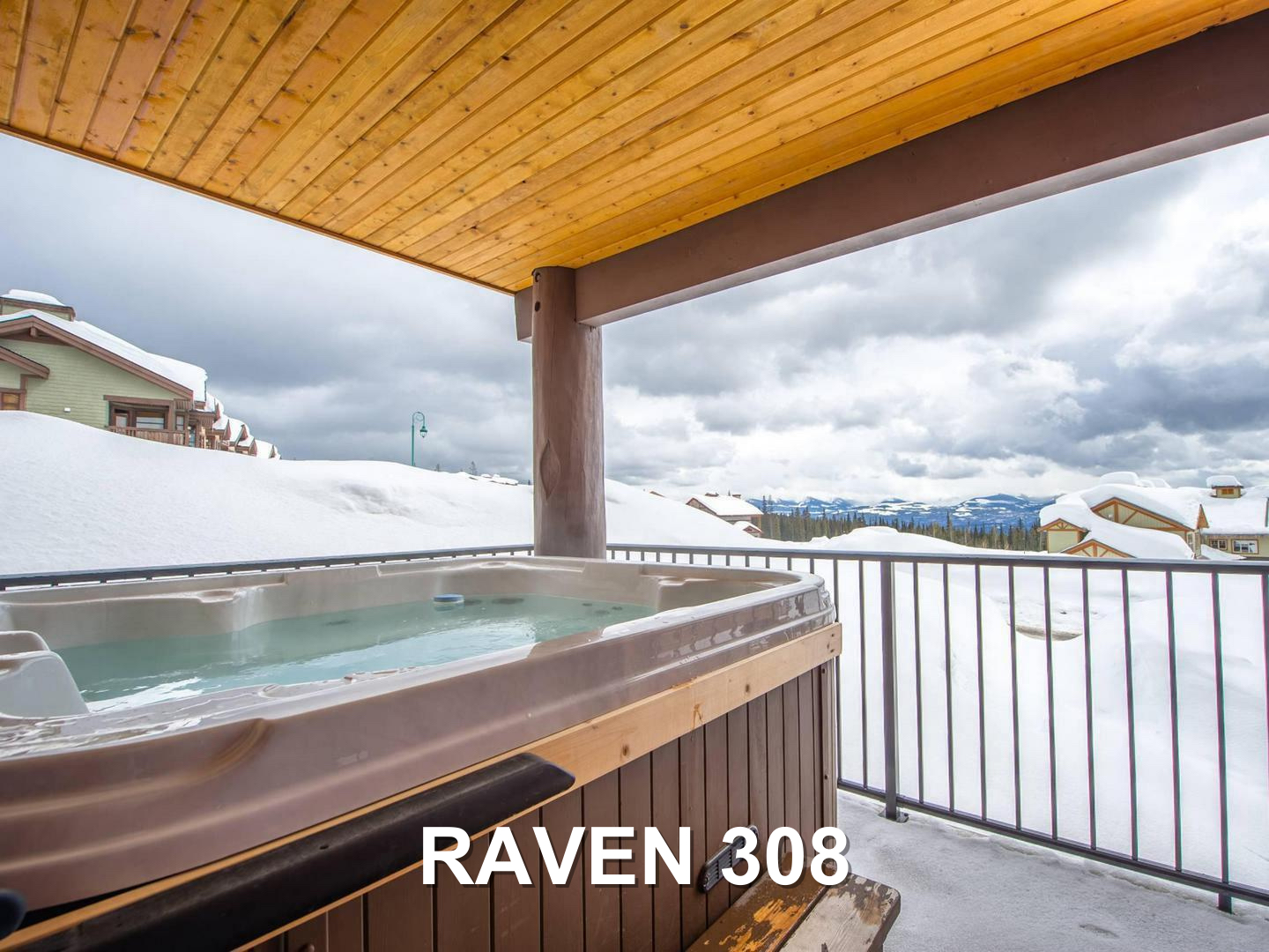 The Raven 308 private deck with the private hot tub overlooking a snowy landscape, located at Big White Ski Resort and managed by Luxury Mountain Vacation Rentals.