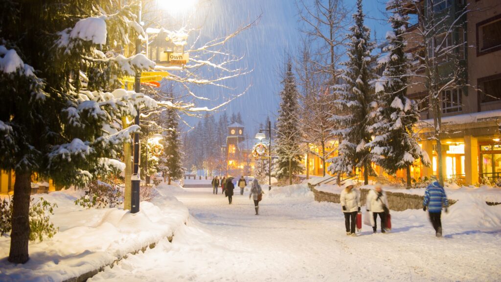 A group of people walk the snowy streets of Whistler Village at night at Whistler Blackcomb Ski Resort.