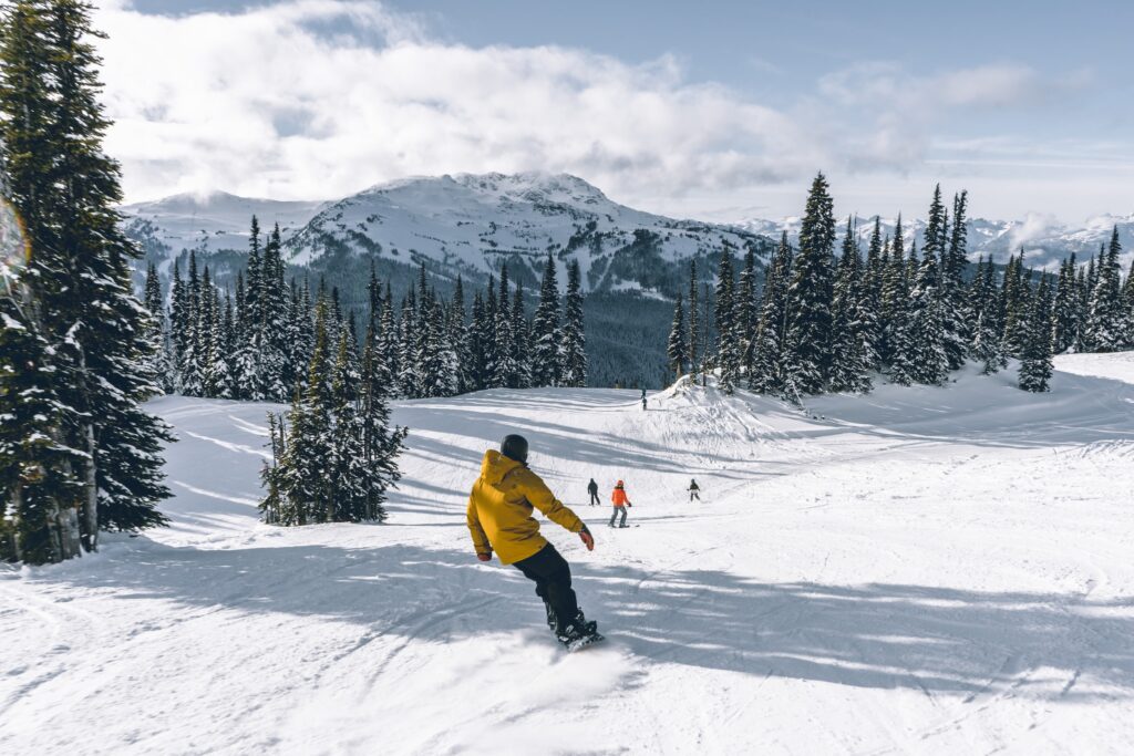 A snowboarder in a yellow jacket snowboards at Whistler Blackcomb Ski Resort on a cloudy day.