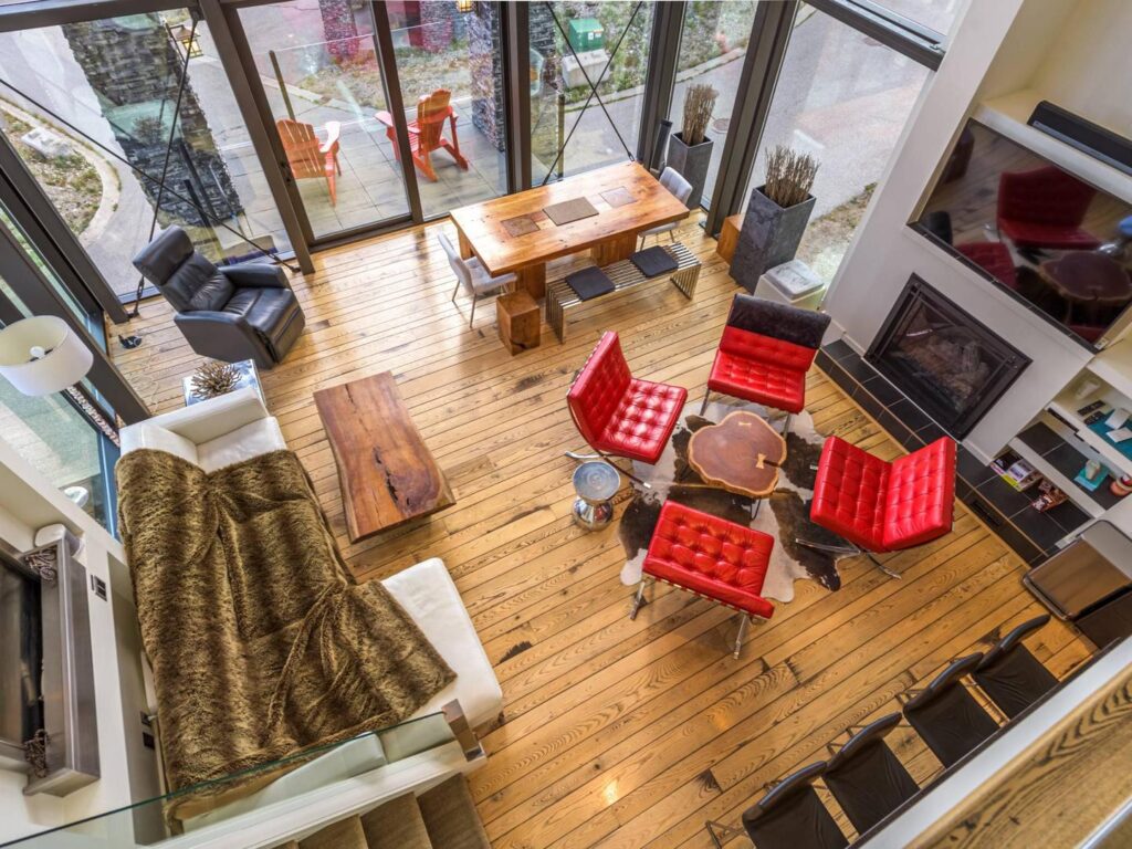An overhead view of a modern living room with red leather chairs, rustic fur blankets, hardwood floors and floor to ceiling windoes in one of the Edge properties, a ski vacation rental from Luxury Mountain Vacation Rentals at Big White Ski Resort.
