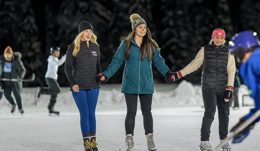 A group of people in winter gear are ice skating at Big White's outdoor ice rink.