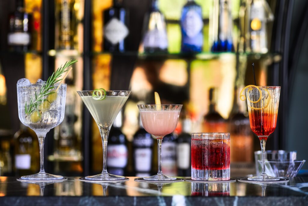 A row of five different cocktails at a fancy bar at night.