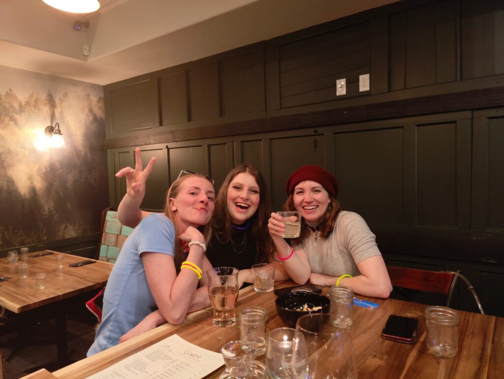 Three LMVR Luxury Mountain Vacation Rentals staff members smiling and posing while sitting at a restaurant pub table at Big White Ski Resort.