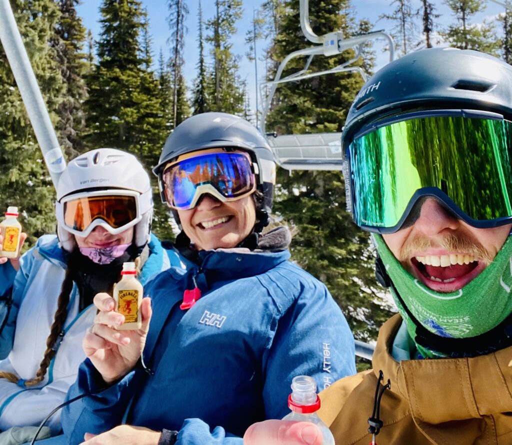 Three LMVR Luxury Mountain Vacation Rental staff members in ski and snowboarding gear smiling together and posing for a staff photo outside at Big White Ski Resort.