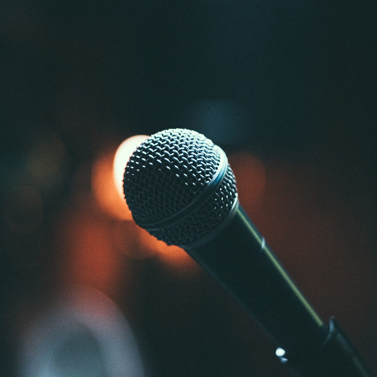 An up-close shot of a stand up comedy microphone on stage with dark lighting in the background.