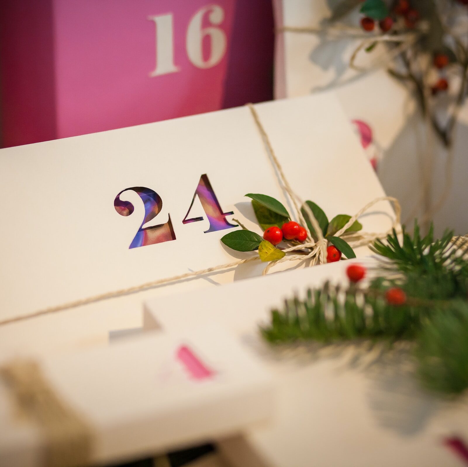 An Advent Calendar style set of boxes in pink and white, with the 24th box in the centre and pieces of holly around it to celebrate Christmas Eve.