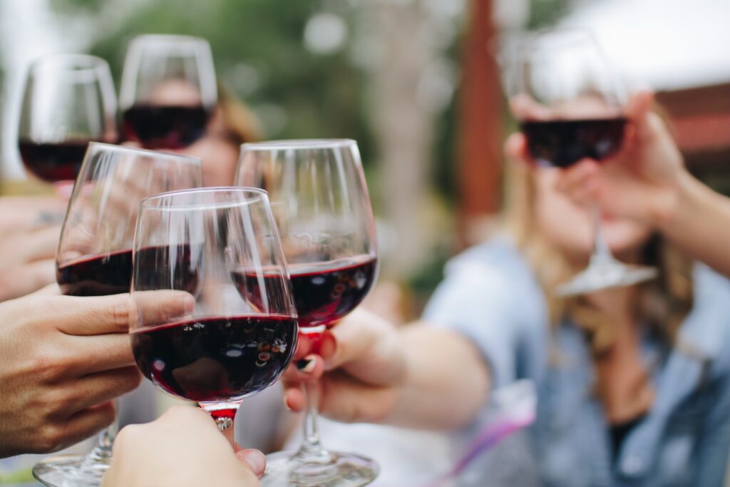 A group of friends cheers each with their our wine glass filled with red wine while outside during a private sommelier wine tasting. 