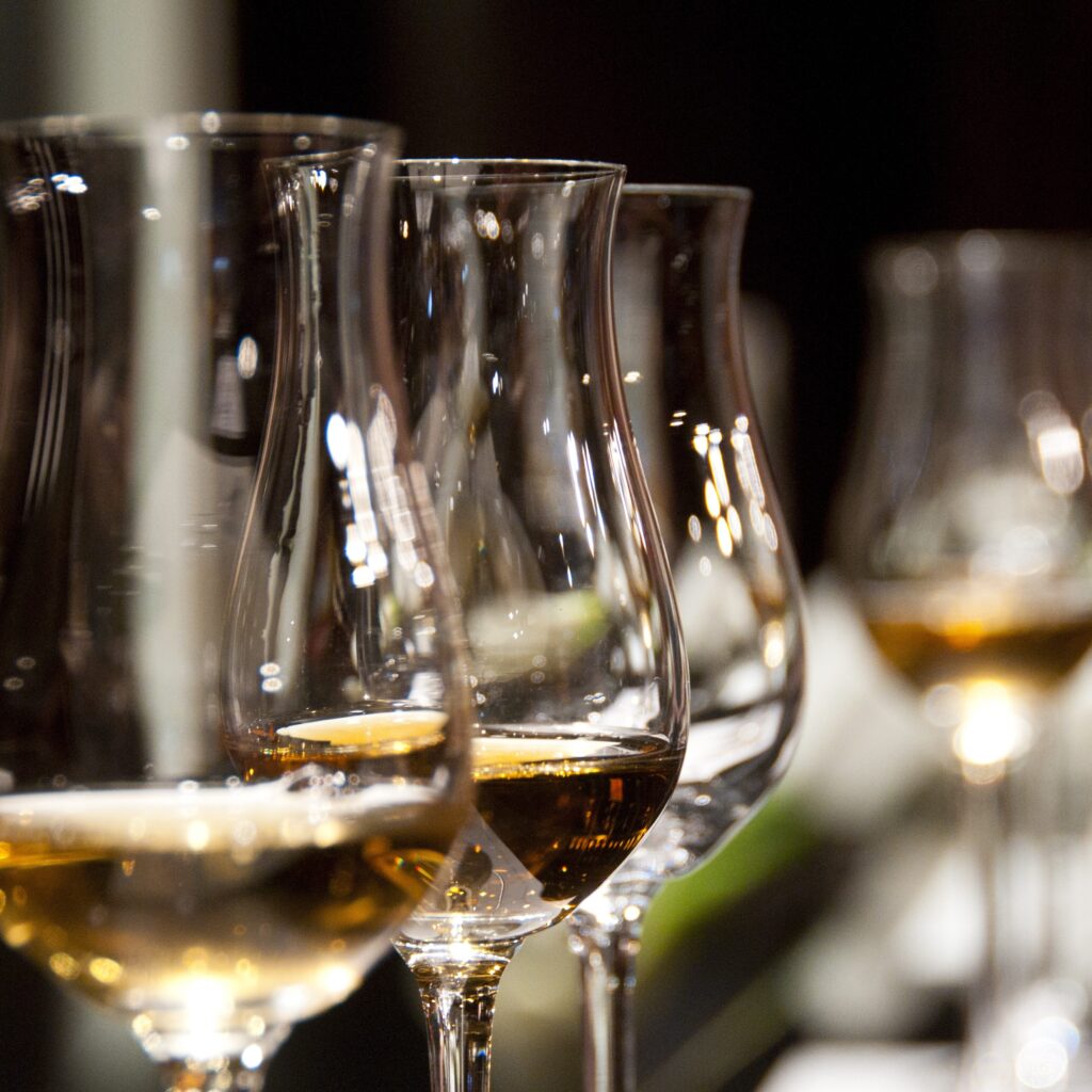 A set of curved wine glasses sit arranged in a line on a bar with a blurred background, set up for an expert sommelier private tasting with LMVR.