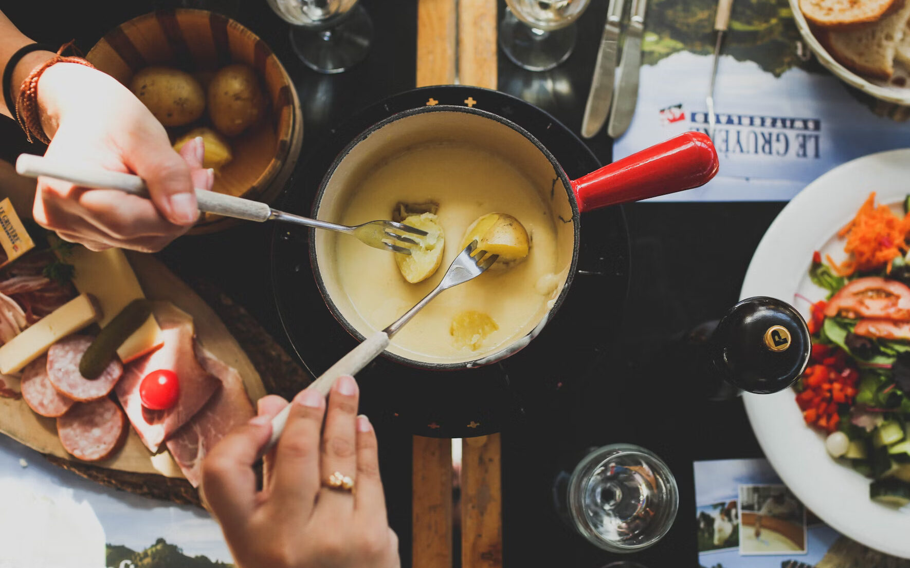 Two people dipping potatoes into a cheese fondue pot.