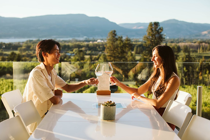 A couple enjoying a wine tasting at Tantalus Vineyards with Okanagan Lake views.